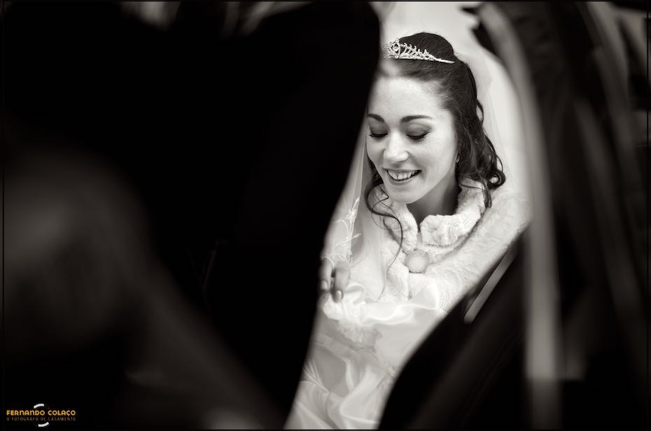 Rosto da noiva sorrindo emoldurado pelas portas escuras do automóvel quando chega ao local da cerimónia, numa composição do fotógrafo de casamento em Almada.