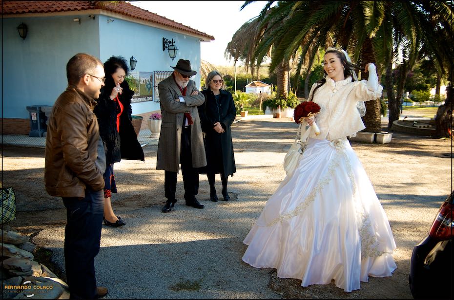 Junto de alguns convidados do casamento, a noiva, de pé, sorri para eles ao chegar para a cerimónia do casamento na Quinta do Joinal.