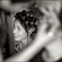 Vista no meio de elementos muito desfocados, a noiva, com rolos no cabelo, sorri para alguém num momento captado pelo fotógrafo de casamento em Sintra.