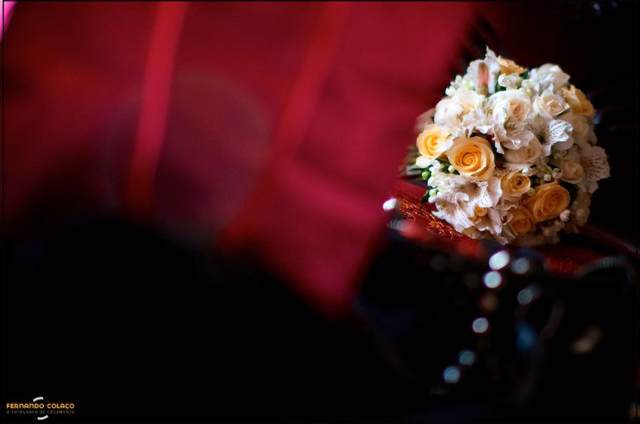 O ramo da noiva sobre uma pequena mesa, emoldurado por panos vermelhos desfocados numa composição do fotógrafo de casamento em Cascais.