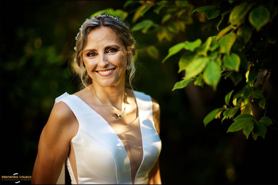 Retrato da noiva, sorrindo, junto das ramagens de uma árvore do jardim da Quinta da Serra, pelo fotógrafo de casamento em Sintra.