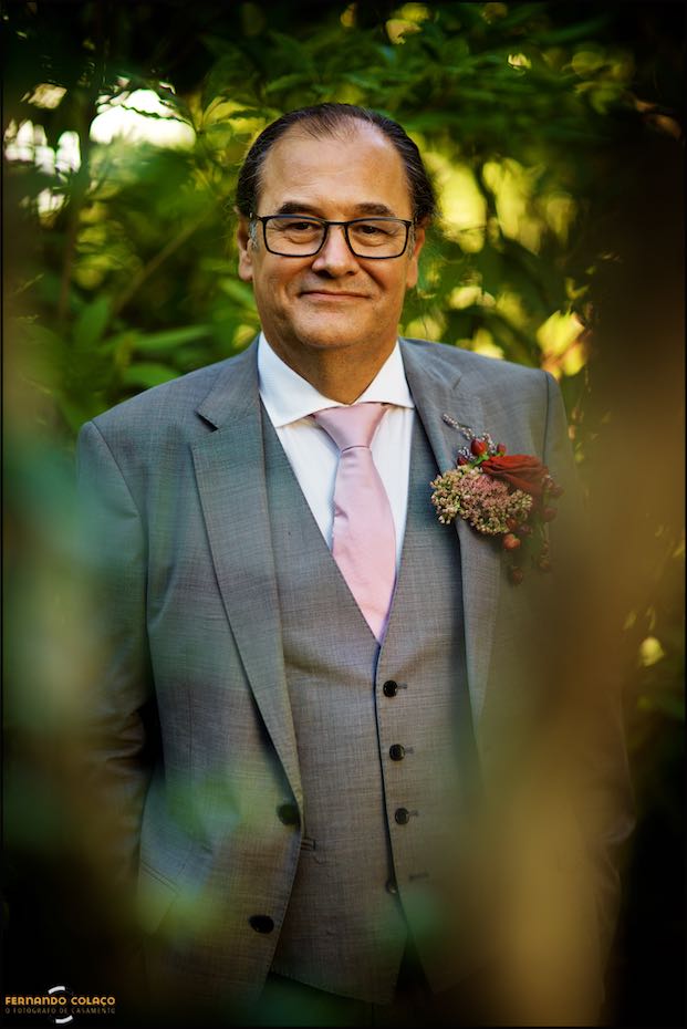 O noivo, sorrindo, no meio dos ramos de árvores do jardim da Quinta do Pé da Serra em Sintra, visto pelo fotógrafo de casamento em Sintra.
