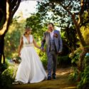 Entre as grandes árvores do jardim da Quinta do Pé da Serra, os noivos passeiam de mão dada, sorrindo e olhando um para o outro, vistos pelo fotógrafo de casamento em Sintra.