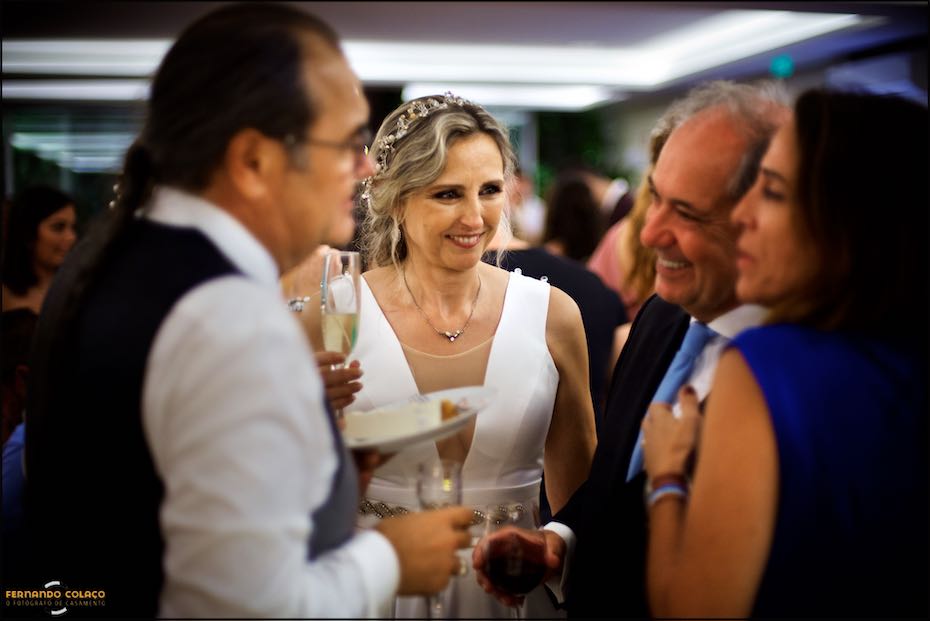 A noiva no meio do noivo e dois convidados com quem conversam, depois do corte do bolo na Quinta do Pé da Serra em Sintra, vistos pelo fotógrafo de casamento.
