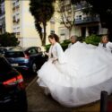 The bride arrives by the car to go to the wedding ceremony, with her mother and two aunts holding the tail of her dress.