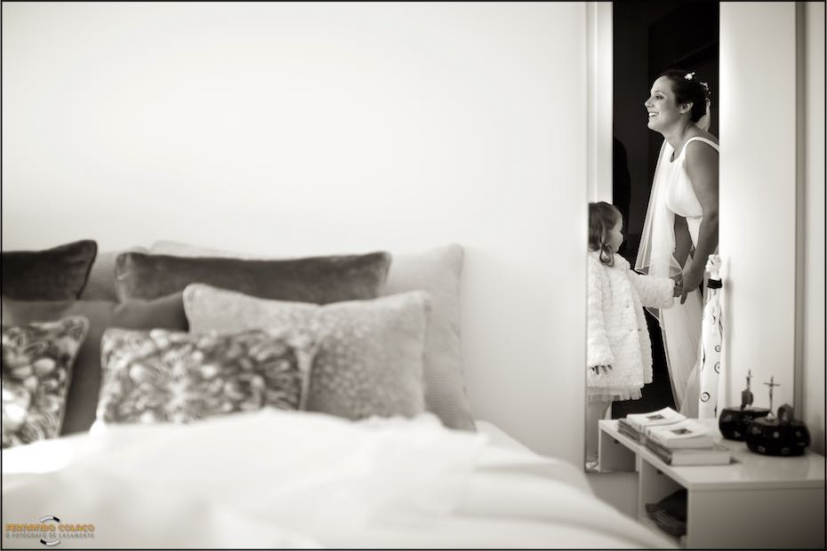 A girl helps the bride hold a box containing the wedding rings, seen through a door by the wedding photographer in Seia, Serra da Estrela.