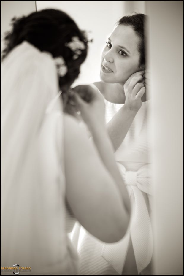The bride, in the mirror, puts on one of her earrings, seen by the wedding photographer in Seia.