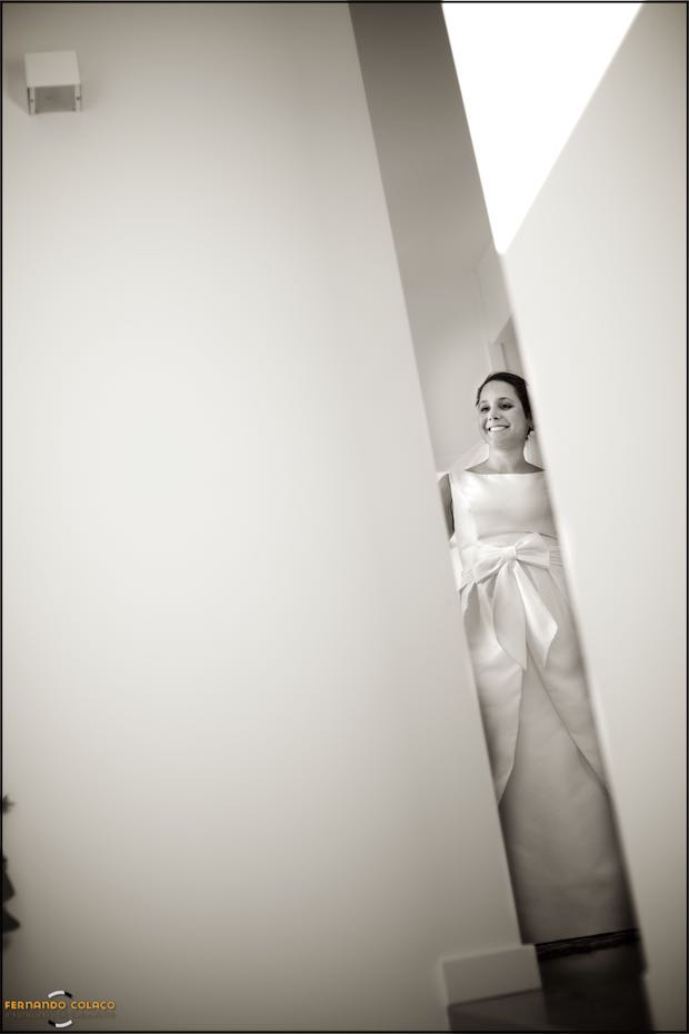 The bride, smiling and wearing her dress, ready to go to the wedding ceremony, seen by the wedding photographer in Seia, between two walls at the top of the stairs.