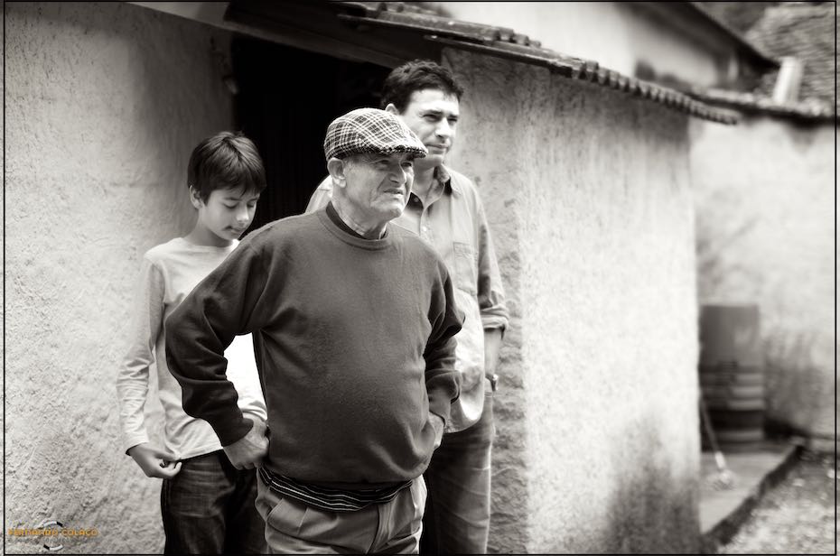 The groom's father, with two young men, out of focus, behind him while listening to a conversation, seen by the wedding photographer in Fátima.