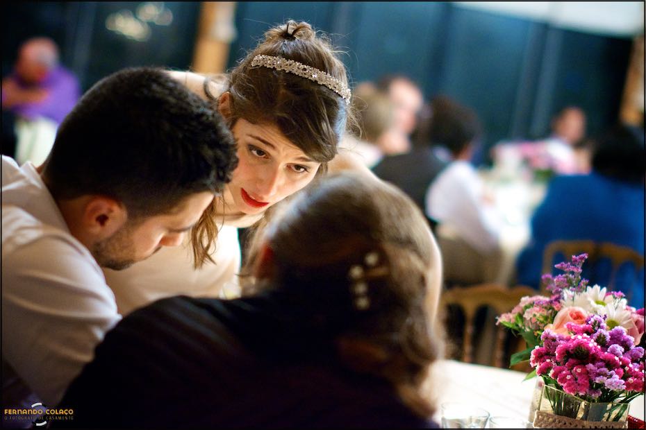 Seen between two guests, the bride talks to them at the wedding dinner table at Quinta de Nossa Senhora da Serra in Sintra.