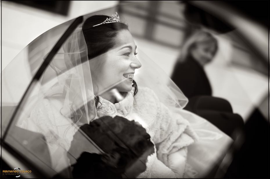 Already sitting in the car, the new bride laughs with satisfaction moments before leaving for the ceremony, as seen by the wedding photographer in Almada.