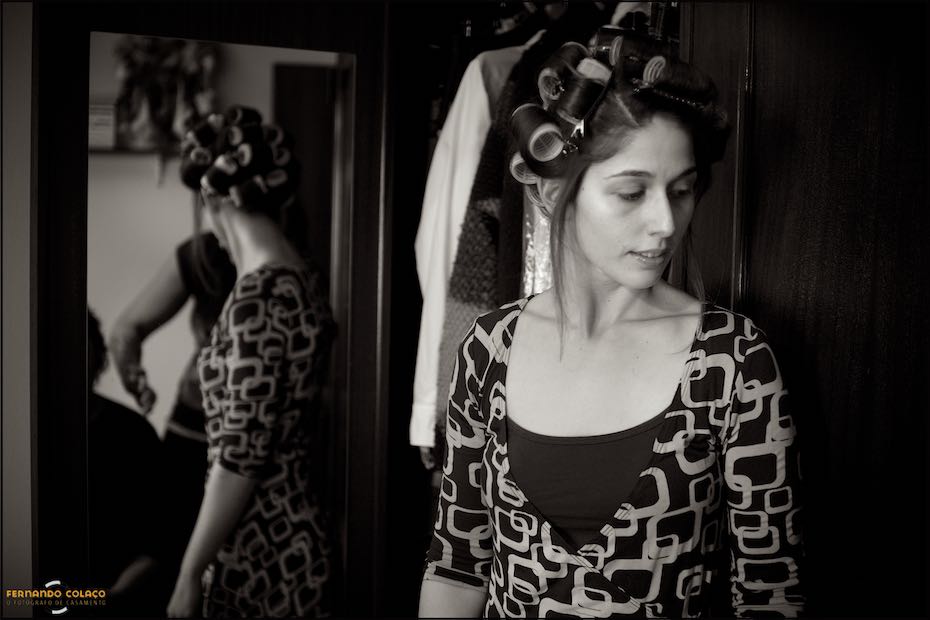 The bride looks away, her back to a mirror on a piece of furniture, with rollers in her hair as she gets ready for her wedding day at Quinta de Nossa Senhora da Serra in Sintra.