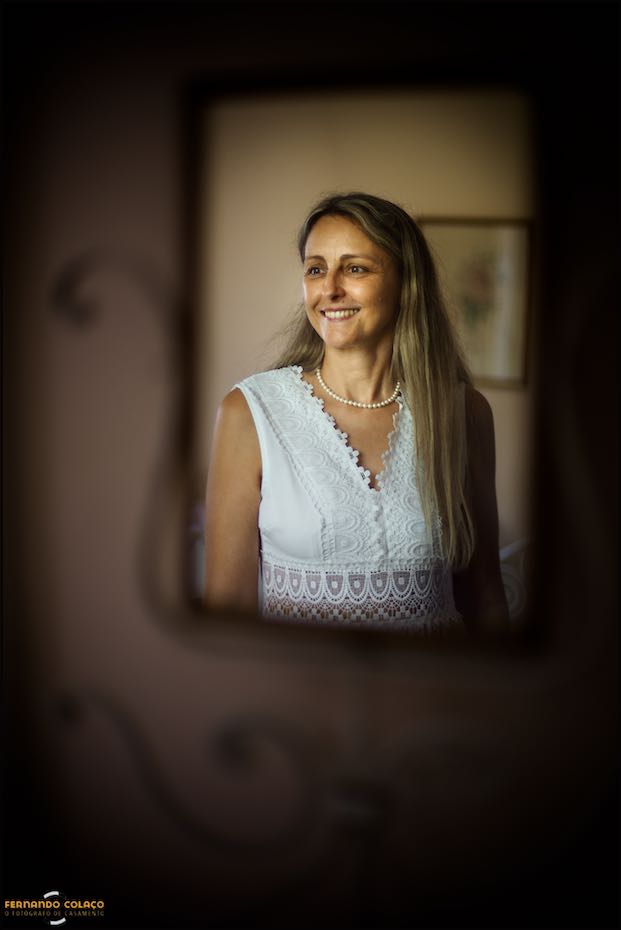 In a mirror in the old house at Quinta do Pé da Serra, the bride smiles in a portrait by the wedding photographer in Sintra.
