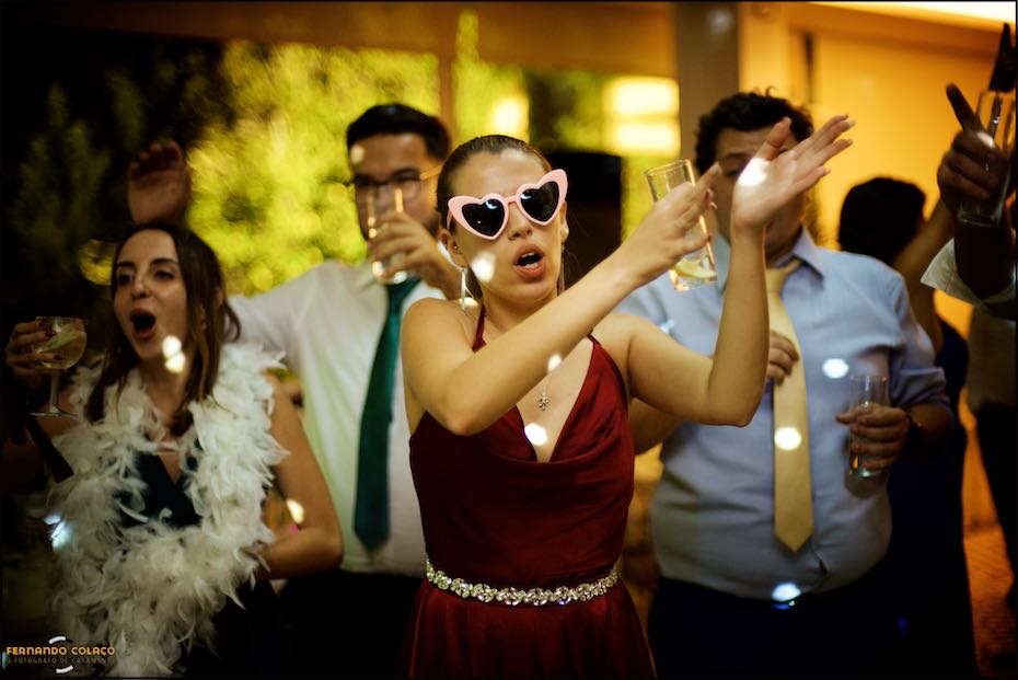 A female guest at the wedding at Quinta do Pé da Serra, wearing heart-shaped glasses, dancing among others, seen by the wedding photographer in Sintra.