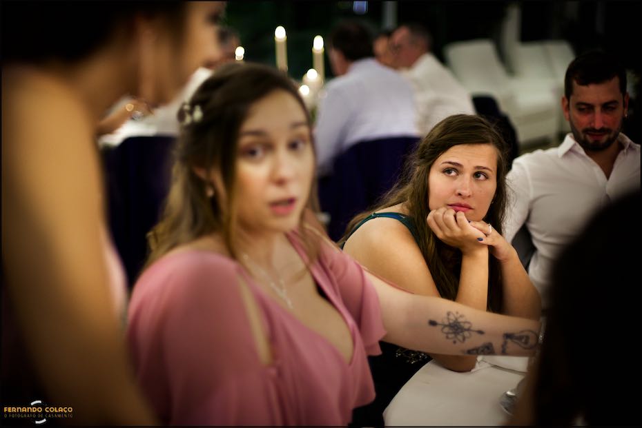 At a dinner table in Quinta do Pé da Serra, friends chat while one of them listens intently, as captured by the wedding photographer in Sintra.