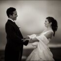At dusk in Casa de Reguengos, the bride and groom hold hands and face each other, smiling at the clouds in the background, as seen by the wedding photographer in Lisbon.