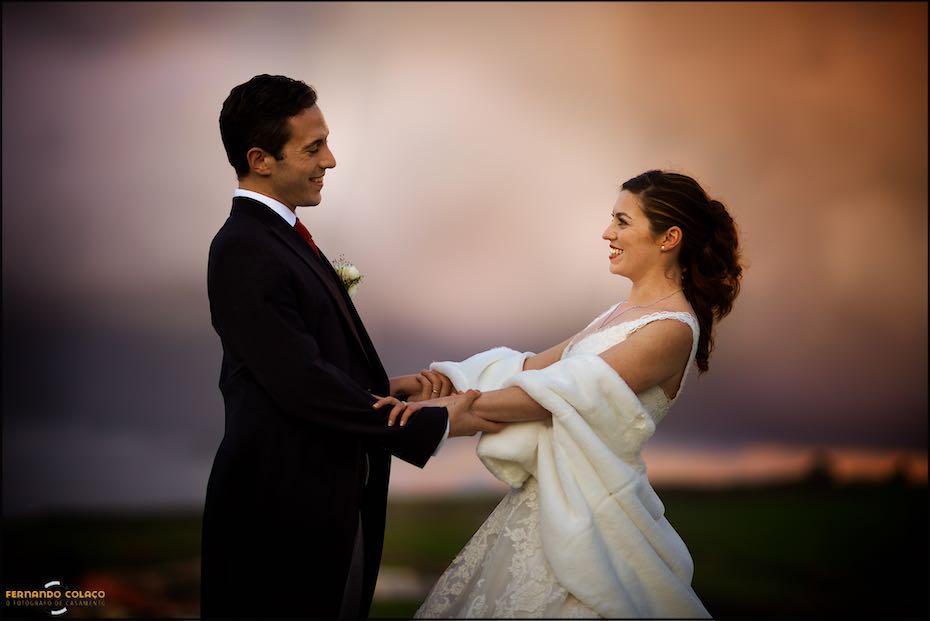 In the light after sunset, the bride and groom are facing each other, holding hands and laughing, as photographed by their wedding photographer in Lisbon.